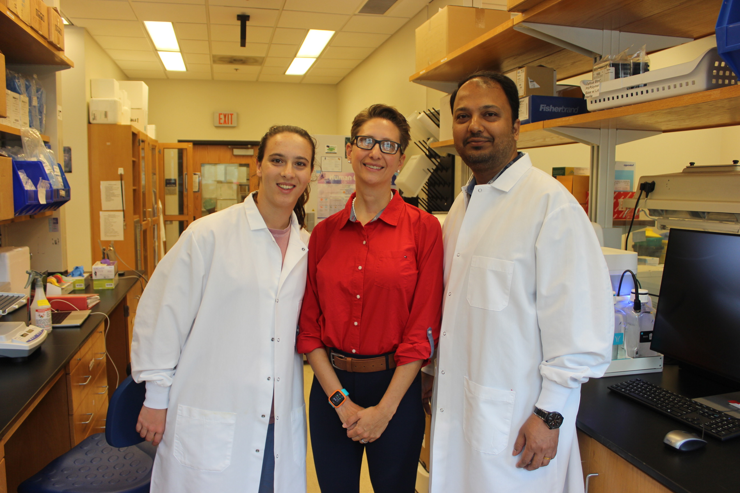 Three people standing together in a laboratory surrounded by lab equipment.
