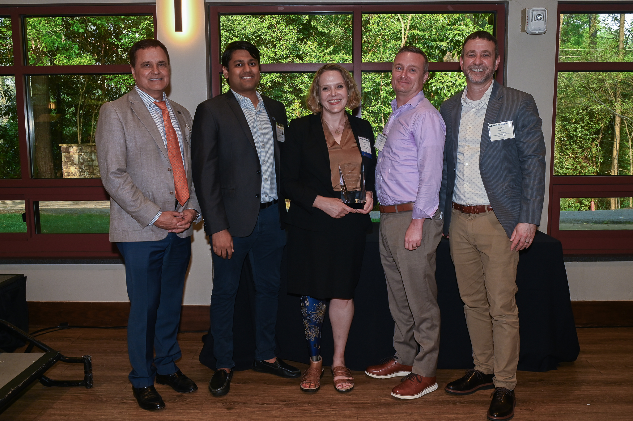 Five attendees pose for a photo, smiling, with one person holding an award.