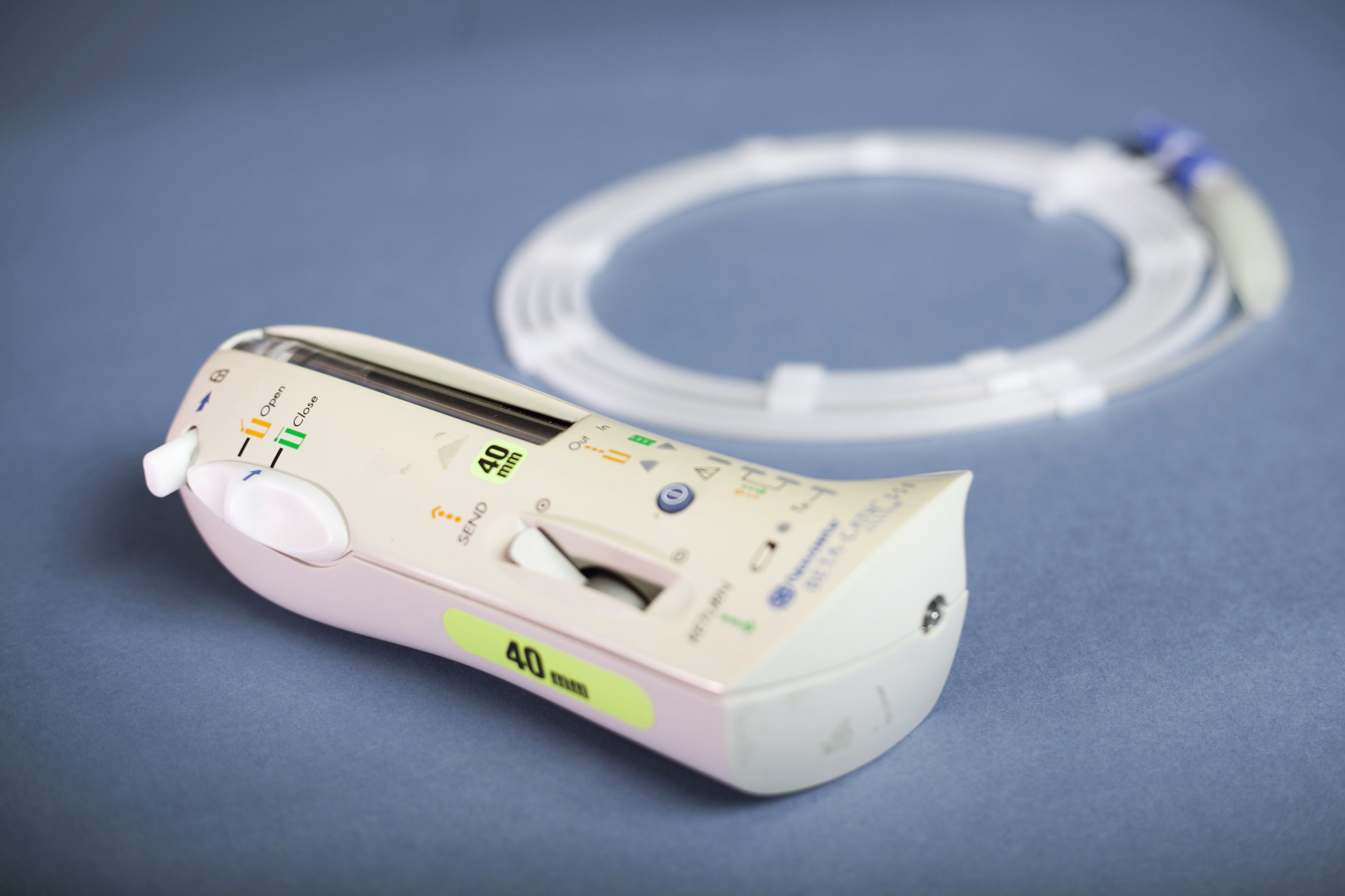 Handheld medical device with labeled controls and a coiled clear tube on a blue surface.