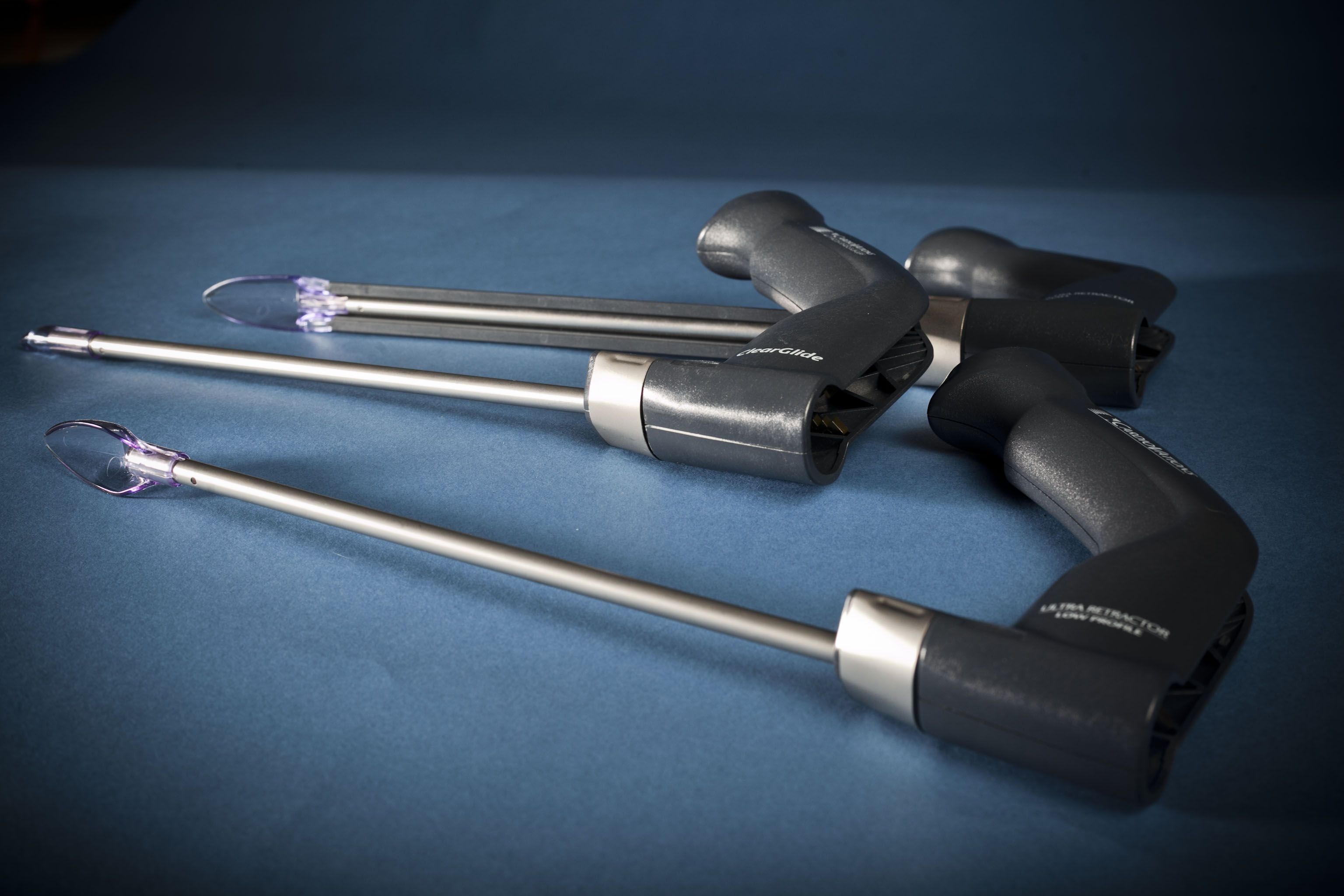 Three black-handled laparoscopic instruments with long metal shafts and looped tips on a blue background.