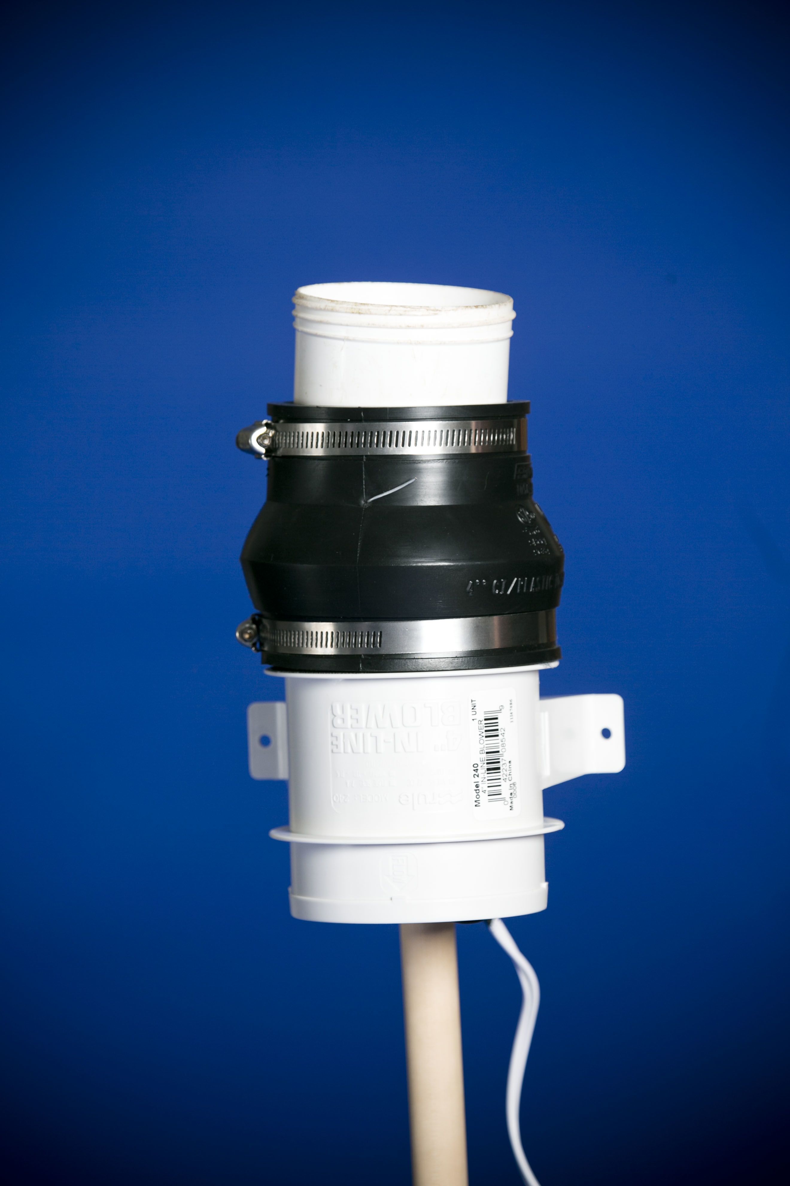PVC pipe connector with black rubber coupling and metal clamps, mounted vertically against a blue background.