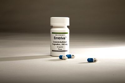 White bottle labeled “Emtriva” with blue-and-white capsules scattered in front on a neutral surface.