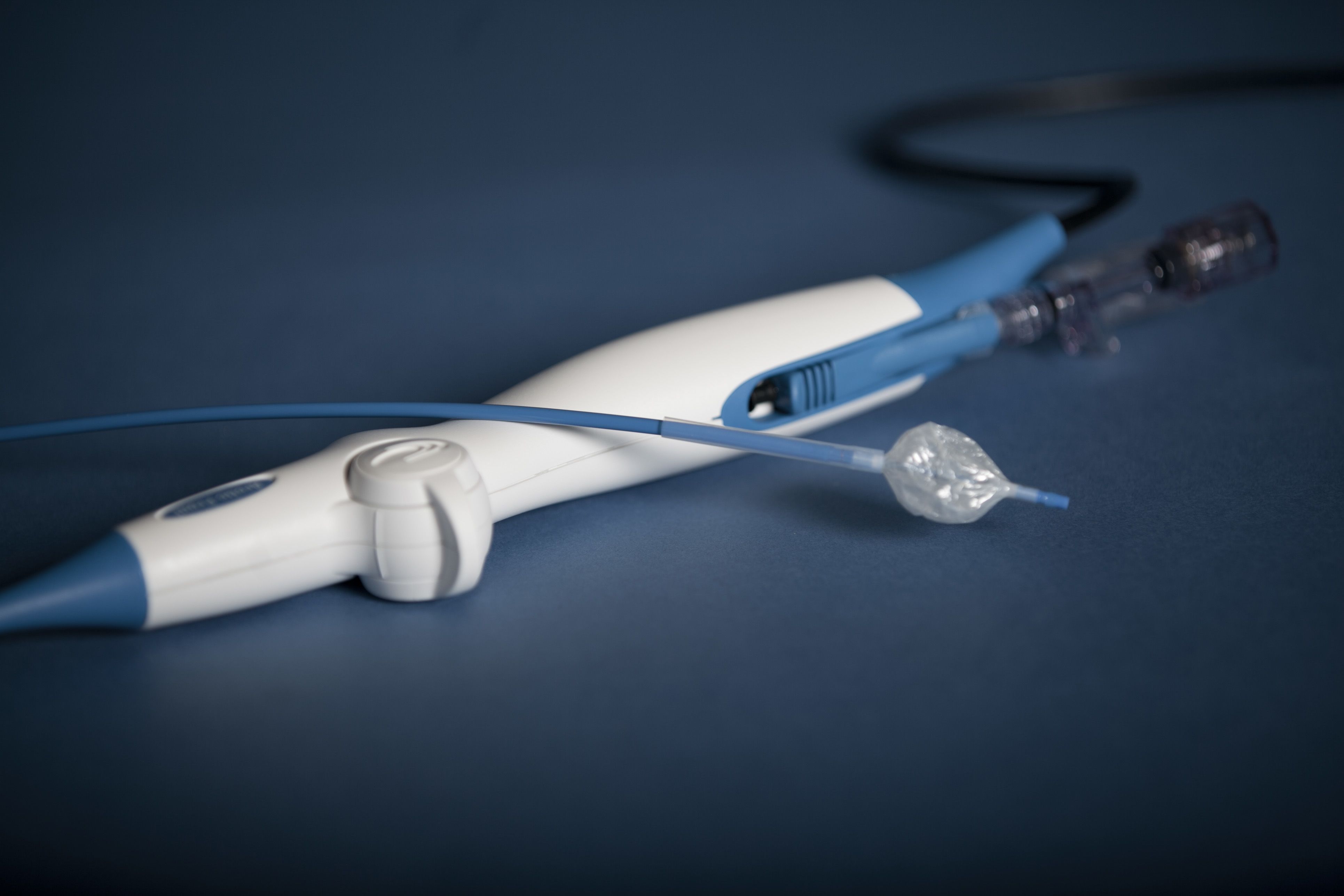 White and blue handheld medical instrument with attached tubing and connectors, placed on a blue surface.