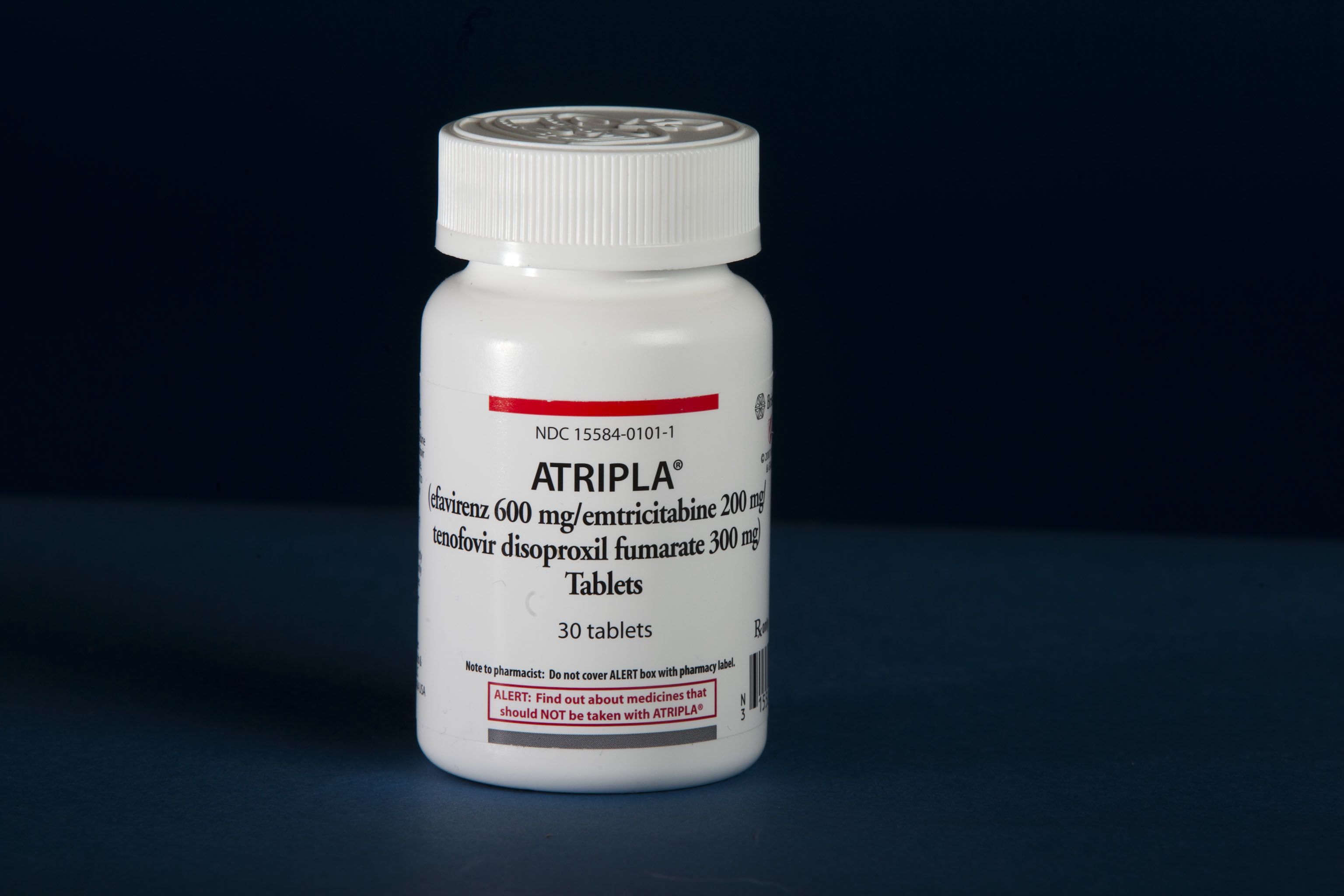 White bottle labeled “Atripla” with dosage details and warning text, placed on a blue surface.